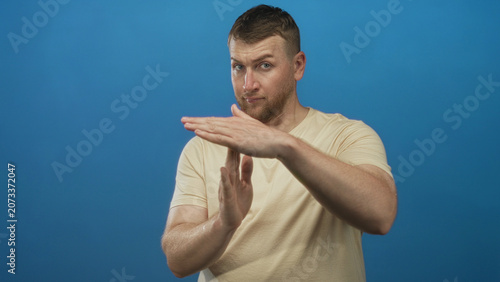Foto Young heavyset man with hands forming timeout gesture in bright blue studio setting, visible forearms and neutral expression; seriousness