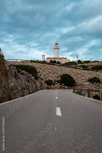 Lighthouse on cliff above road, dramatic blue sky