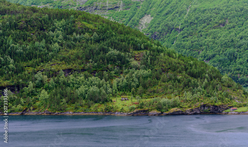 Geiranger, Majestic Norwegian Fjord Landscape, Dramatic fjord landscape with steep, green mountains and calm water under a cloudy sky. Serene natural beauty.