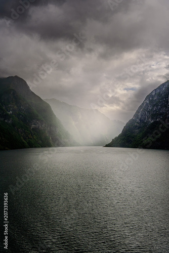 Geiranger, Majestic Norwegian Fjord Landscape, Dramatic fjord landscape with steep, green mountains and calm water under a cloudy sky. Serene natural beauty.