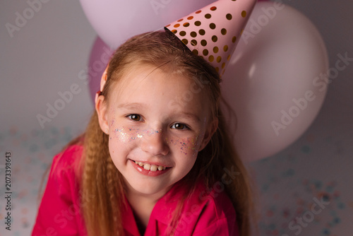 happy little girl with pink balloons and glitter on her face in a studio, celebrating her birthday. space for text