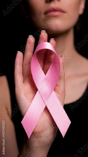 A woman's hand holds a pink ribbon, a symbol of awareness and support. A black backdrop