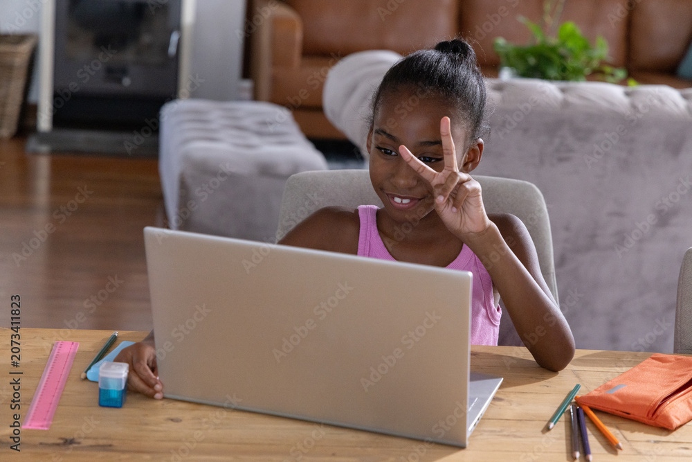 Obraz premium African American girl child wearing pink top sitting at table in living room using silver laptop
