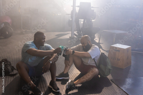 Canvastavla African American men clinking shaker bottles while resting on rubber gym floor i