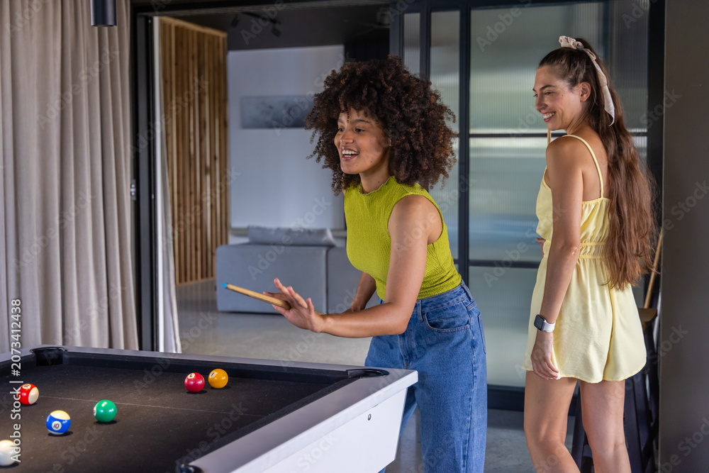 Obraz premium Diverse female friends playing at black pool table in lounge, shooter in lime top holding cue
