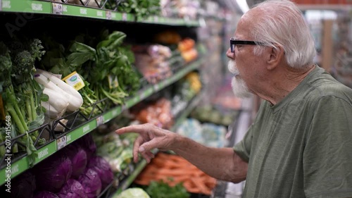 Happy elderly man selects fresh fruits and vegetables in a grocery store. He enjoys shopping and choosing healthy food.