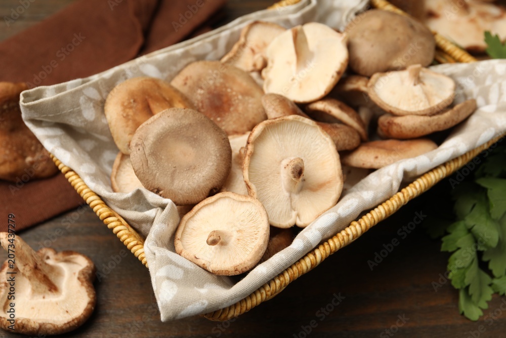 Fototapeta premium Raw shiitake mushrooms in wicker basket on wooden table, closeup
