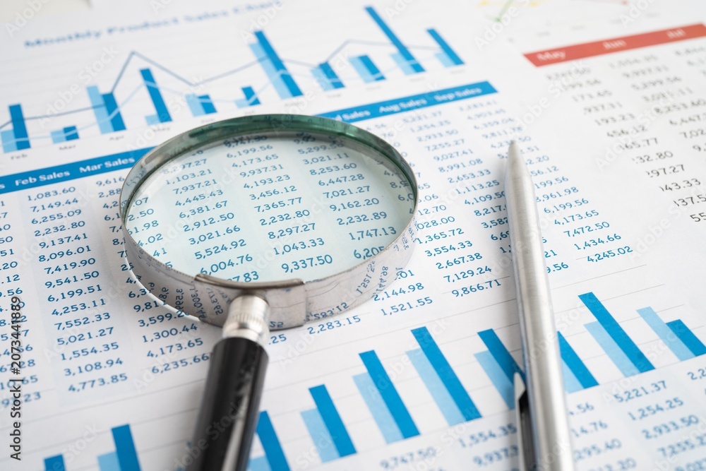 © mrzn - Close up view of magnifying glass over financial spreadsheet and bar charts for detailed business data inspection with analysis