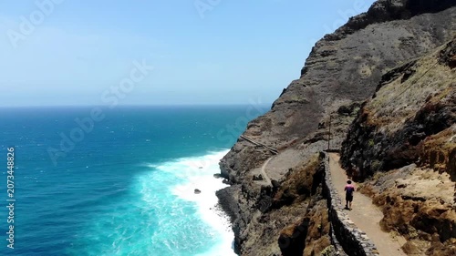 Cinematic aerial shot of a person hiking along the dramatic coastal trail of Santo Antão, Cape Verde