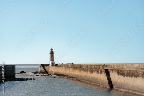A solitary lighthouse rises majestically beside calm waters, with a gentle breeze sweeping across the pier