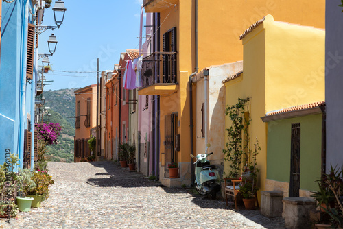 Picturesque, narrow cobblestone alley in Bosa, Picturesque, narrow cobblestone alley in Bosa, Sardinia, featuring iconic, brightly colored houses in shades of yellow, blue, and orange, adorned with po