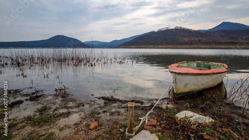 Foto Old wooden fishing boat tied to a wooden post on a lake shore with rolling hills
