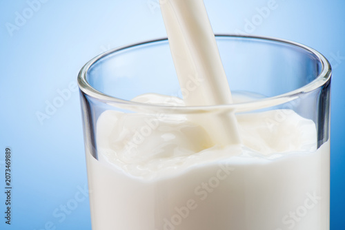 Fotografie Fresh milk pouring into transparent glass on blue background