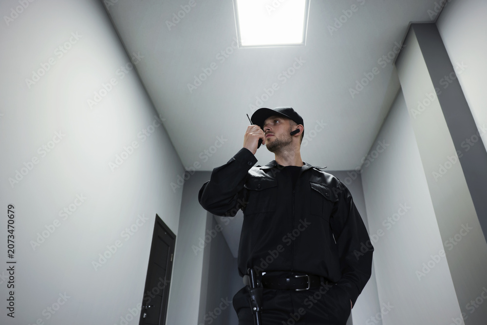 Obraz premium Bodyguard in uniform using walkie talkie indoors, low angle view