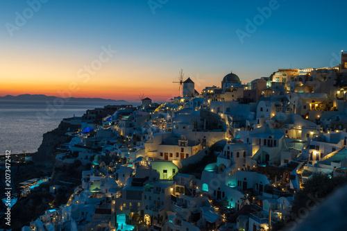 Tableau sur toile Illuminated whitewashed houses and church domes in Oia, Santorini, overlooking the Aegean Sea at blue hour with colorful sunset horizon