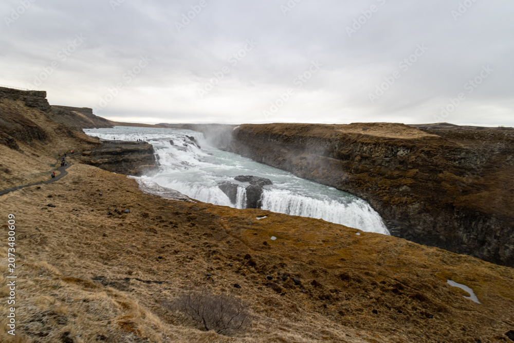 Obraz premium Gullfoss waterfall cascading over two tiers into a deep river canyon under overcast spring skies along the Golden Circle route in Iceland