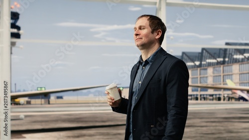 Obraz na plátně Close up of smiling businessman drinking from takeaway coffee cup inside airport terminal, happy man enjoying caffeinated beverage while travelling to plane boarding gate for airport travel