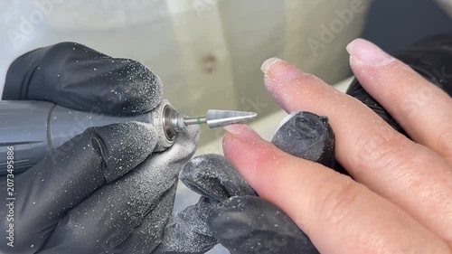 Old chipped gel coating removed from neglected nails by manicurist wearing dark protective gloves while machine softly files surface inside modern nail salon.