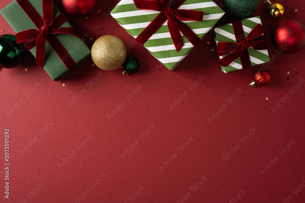 Fototapeta premium Festive Christmas presents and ornaments on red background with green striped wrapping and ribbons