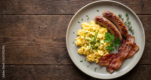 English breakfast flat lay with scrambled eggs sausages and bacon on rustic wood