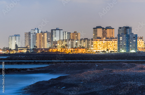 Blue Hour Coastal Landscape with Rocky Shore and Glowing City Skyline