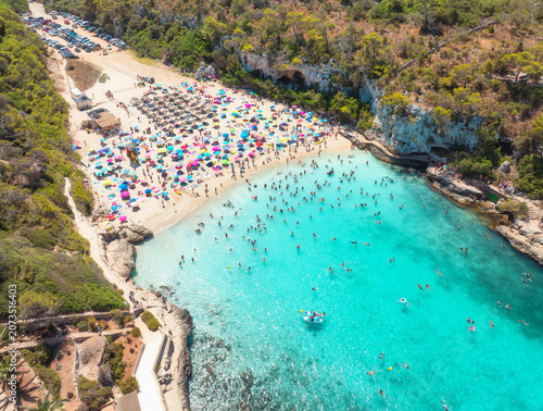 Fotografie Aerial view of colorful umbrellas on crowded sandy beach, swimmers in blue sea, green trees on sunny summer day
