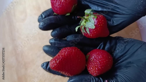 Fresh strawberries held by hands wearing black gloves on wooden table  