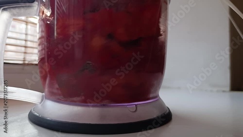 Blending red strawberries in a blender on a white kitchen countertop.
