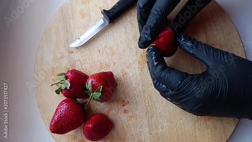 Person wearing black gloves preparing strawberries on wooden cutting board  