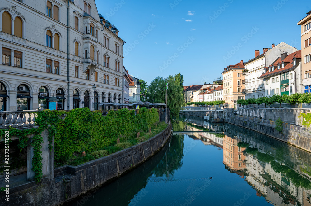 Obraz premium Architecturally elegant buildings on Ljubljanica River in central Ljubljana, Slovenia, on calm clear summer morning reflected in river's still water.