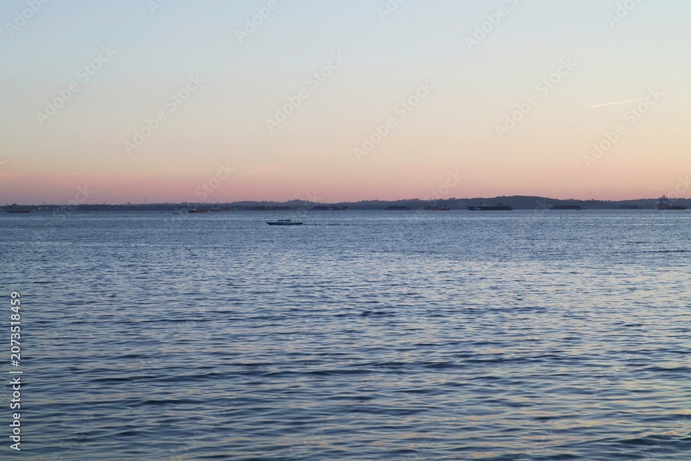Obraz premium A peaceful view of a harbor waterway at dusk with distant vessels.