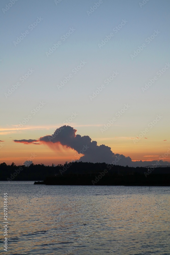 Fototapeta premium Sunset over a calm coastal harbor with dramatic cloud formations.