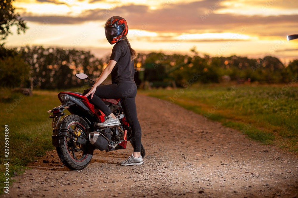 Obraz premium Girl biker resting on motorcycle at sunset on dirt road