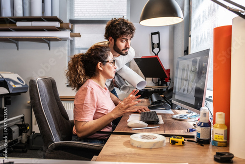 Two colleagues in a print shop work together on preparing a branding project for production. They review designs and print materials, making sure everything is ready before printing.