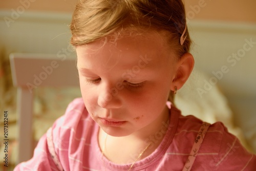 A sad cute small girl. A small girl looks sadly down. A small girl sits in the kitchen.
