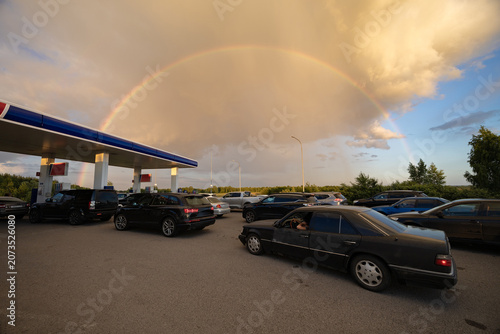 Long queue of cars waits at a gas station on rainbow background