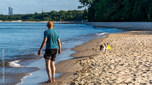 Man walking with dog along sandy beach shoreline