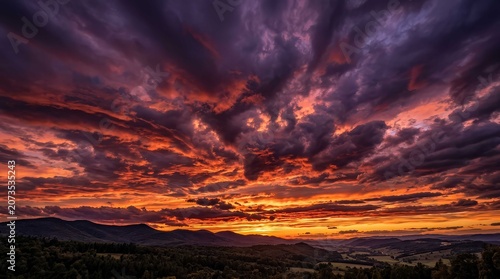 Dramatic sunset landscape with vibrant fiery orange and purple stratocumulus clouds over vast silhouetted mountains, capturing a wide cinematic view of the horizon during the golden hour atmosphere.