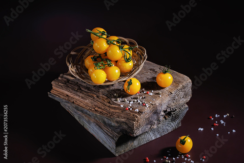 Ripe yellow cherry tomatoes in basket and scattered on wood with mixed spices
