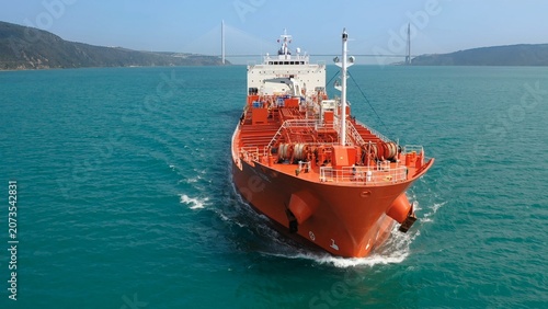 Large red oil tanker ship navigating through Bosphorus, creating a bow wave as it moves forward, with various deck equipment including anchor winches and a mast. Maritime navigation challenges
