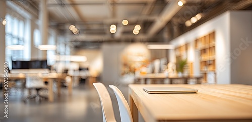 A blurred, modern office space features a wooden table with a laptop, showcasing a bright and collaborative work environment.