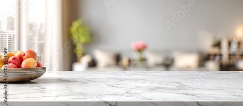 A still life composition featuring fresh peaches in a bowl on a marble countertop with a blurred interior background.