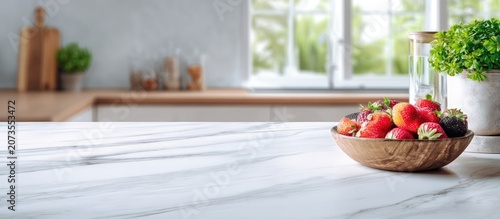 A wooden bowl filled with fresh strawberries and blackberries sits on a marble countertop in a bright, modern kitchen with a window overlooking a lush green garden.
