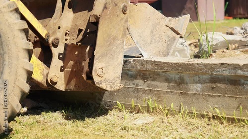 Powerful yellow bulldozer equipped with a front bucket applying force to break and demolish a large concrete block during a construction or demolition project on a sunny day