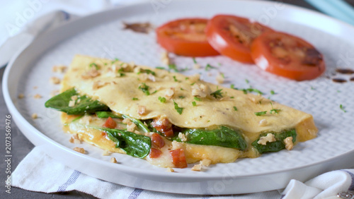 Spinach and cheese omelet with sliced tomatoes on a white plate