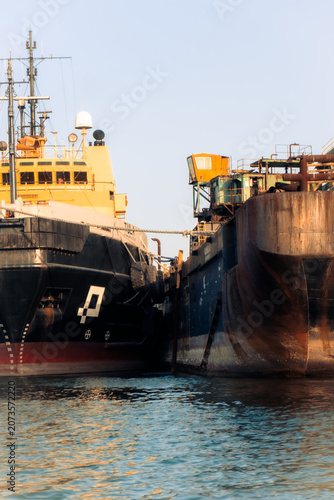 Photos Dockside Diplomacy: Two large ships meet at the dock, their hulls close together, suggesting a connection or transfer in the maritime world