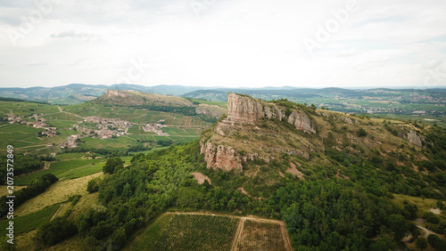 Aerial view of the Rock of Solutre, a limestone escarpment rising above lush green vineyards and rolling hills in Solutre-Pouilly, Bourgogne-Franche-Comte, France.