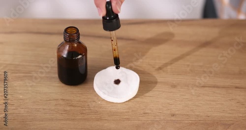 Woman dripping iodine onto cotton disks from pipette at wooden table, closeup