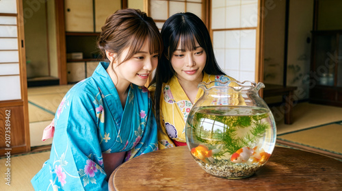 和室のテーブルに置かれた金魚鉢を笑顔で見つめる浴衣を着た女性たち