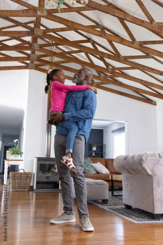 Naklejka premium African American family man holding child girl, smiling in living room with fireplace, wooden beams